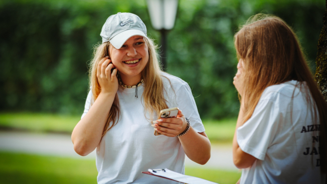 meitene smaida un tur rokās telefonu