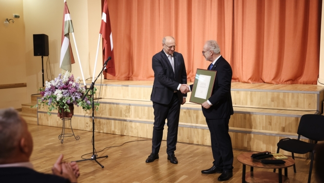 divi vīrieši paspiež rokas, tiek pasniegts goda raksts