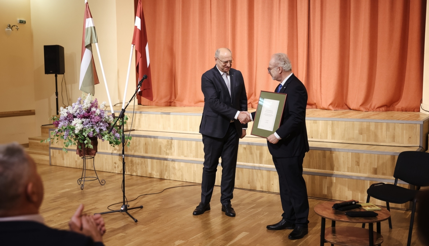 divi vīrieši paspiež rokas, tiek pasniegts goda raksts