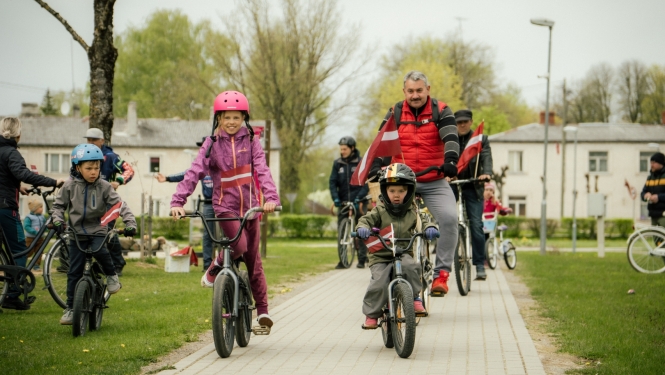 Neretas apvienības pārades vaītājs un bērni 4. maija velo braucienā ar Latvijas karogiem