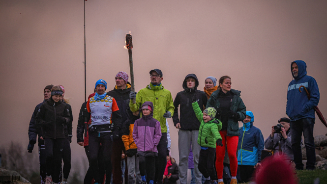 Cilvēki stāv kalnā, vienam no viņiem iedegta lāpa rokās