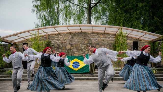 deju kolektīvs dejo ar Brazīlijas karogu fonā