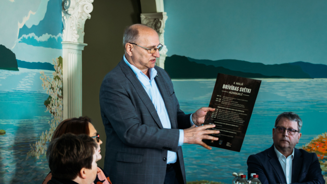 vīrietis tur rokās afišu un rāda uz to