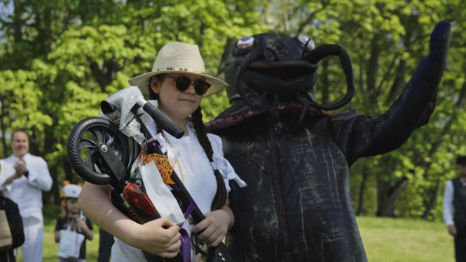 cilvēks sama maskā un meitene ar laimēto skrejriteni