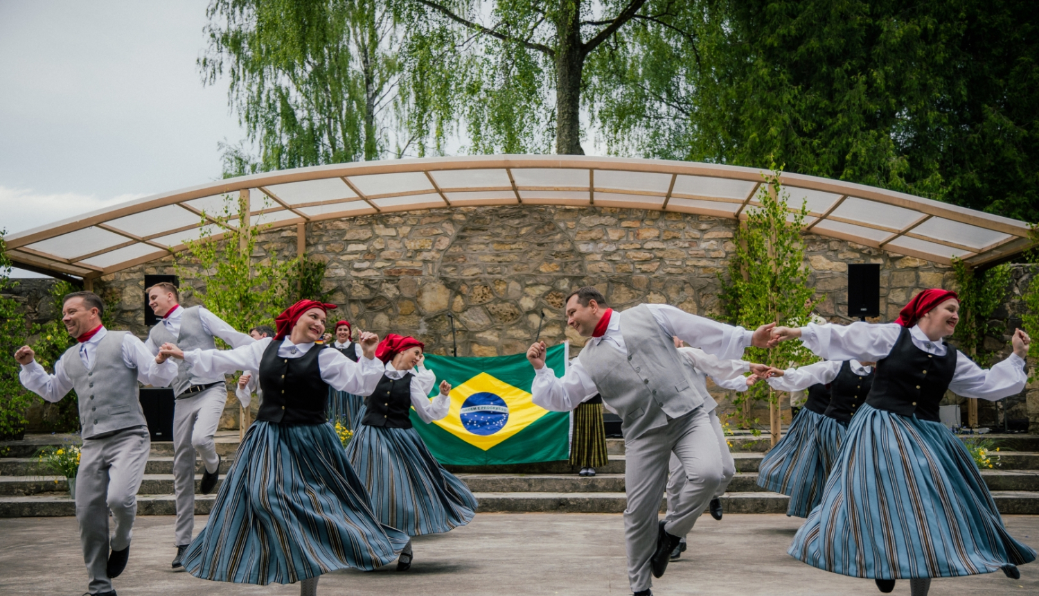deju kolektīvs dejo ar Brazīlijas karogu fonā