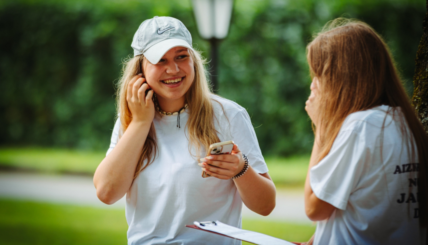 meitene smaida un tur rokās telefonu