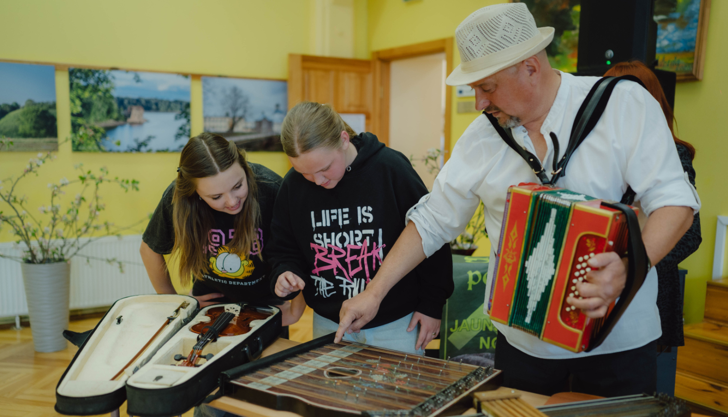 trīs cilvēki skatās mūzikas instrumentus