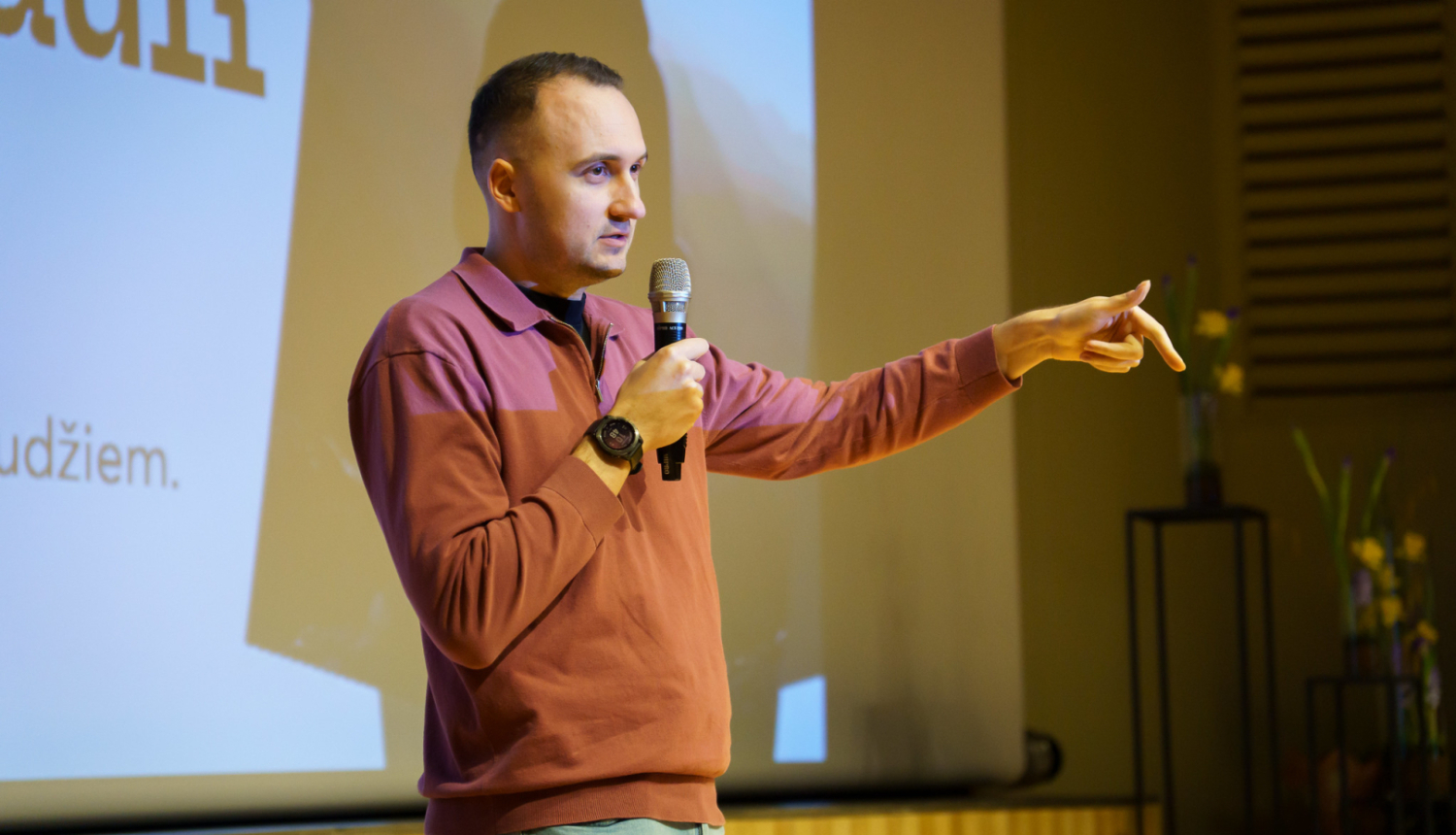 vīrietis runā pa mikrofonu un žestikulē