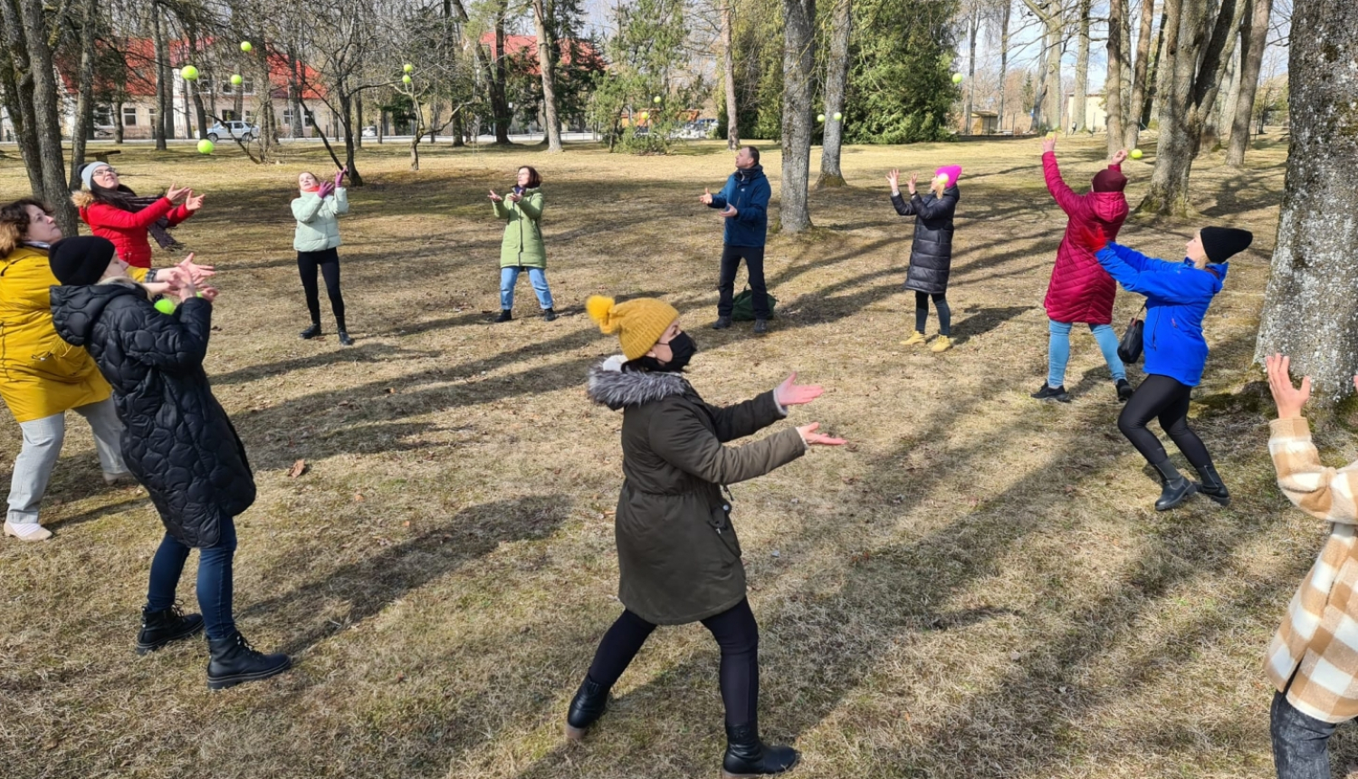 dalībnieki mētā tenisa bumbiņas, stāvot aplī