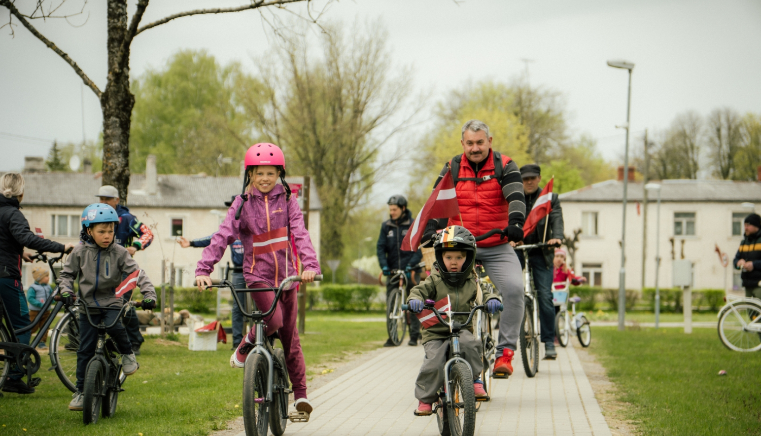 Neretas apvienības pārades vaītājs un bērni 4. maija velo braucienā ar Latvijas karogiem