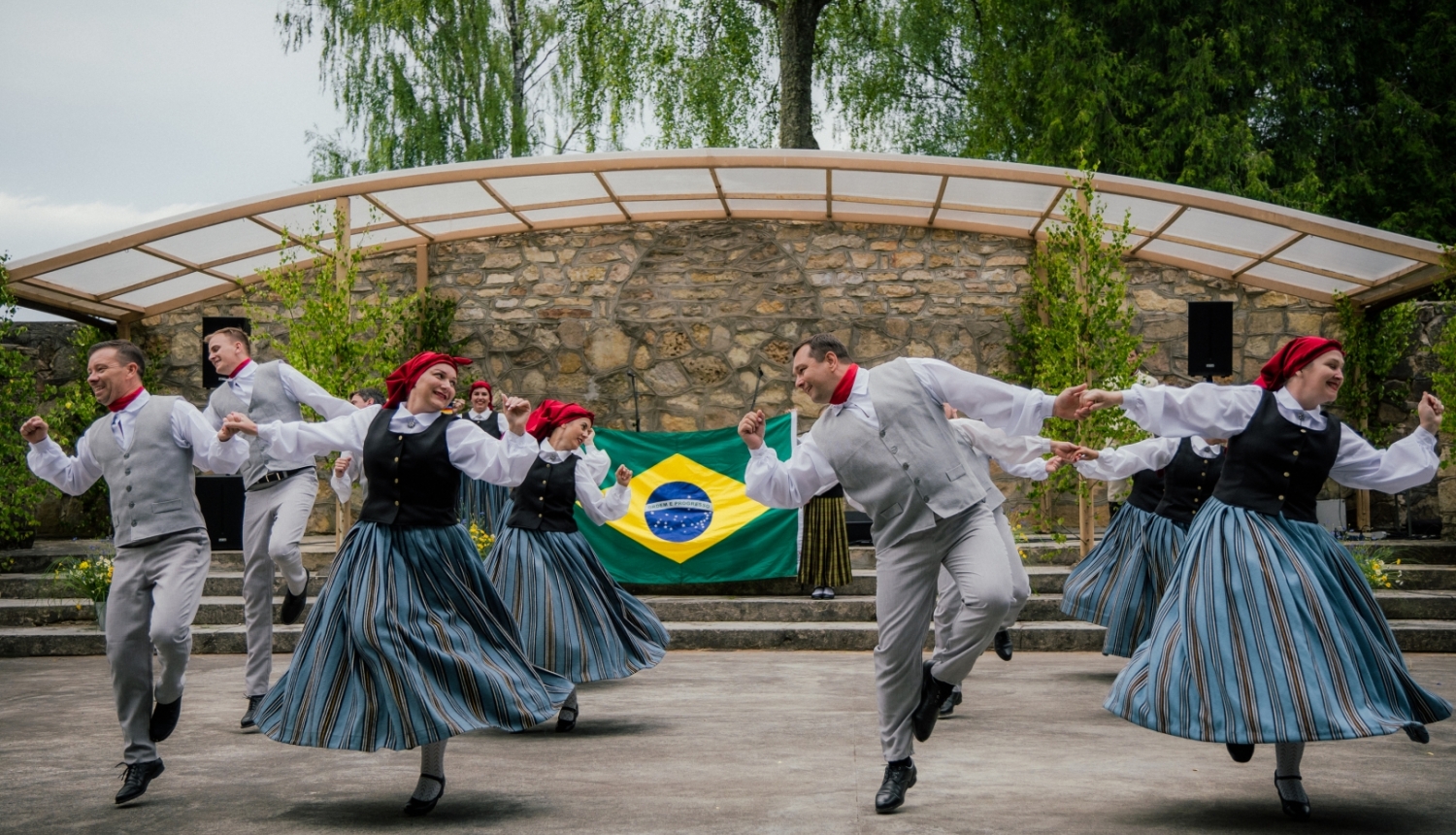 deju kolektīvs dejo ar Brazīlijas karogu fonā